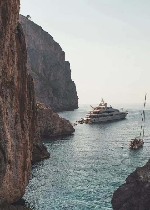 A yacht anchored in a sheltered cove below cliffs in the Balearic Islands